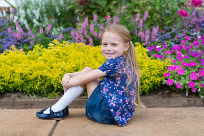 Portrait of cute smiling girl sitting by flowers blooming in yard