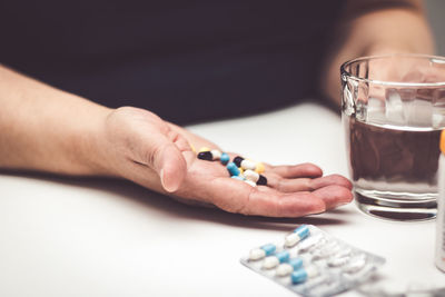 Cropped hands of woman holding pills and drinking water in glass