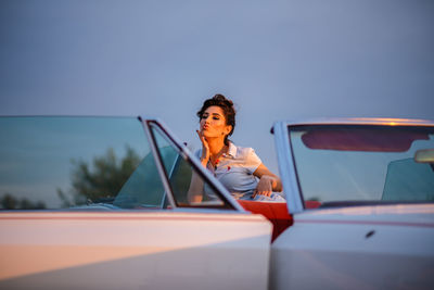 Portrait of woman sitting on car against sky