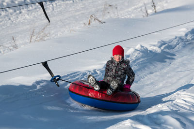 Portrait of boy sitting in inflatable ring on snow covered land