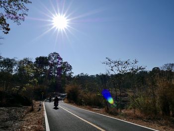 Road by trees against sky on sunny day