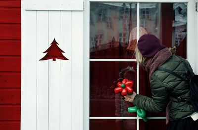 Rear view of woman holding balloon looking through window