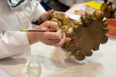Experienced lady restoring a small gilded statuette with a very fine brush in her art studio.
