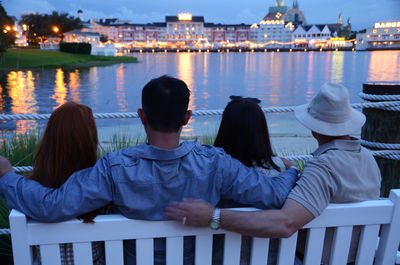 Rear view of friends sitting on railing in city at night