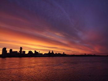 Silhouette city by sea against romantic sky at sunset