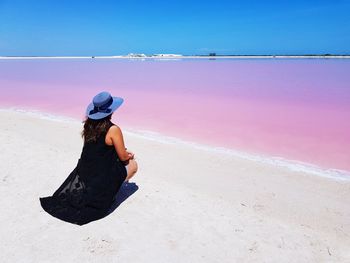 Woman sitting on sand against sea at beach