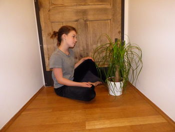 Side view of young woman sitting on potted plant at home