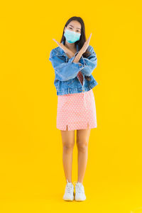 Full length portrait of woman standing against yellow background