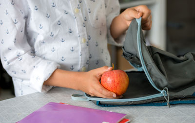 Midsection a boy holding apple with school bag, back to school concept