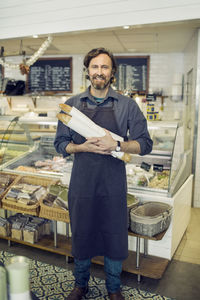 Portrait of mature male baker holding loaves of bread in supermarket