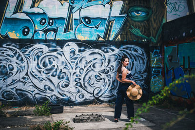 Full length of young woman standing against graffiti wall