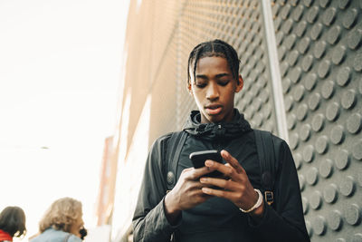 Low angle view of teenage boy using mobile phone while standing in city