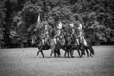 Men riding horses on field against trees