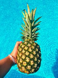 Cropped image of hand holding apple against swimming pool