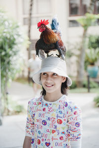 Smiling girl with chicken on head standing on road