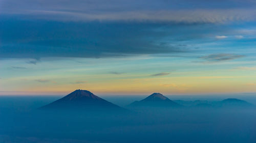 Merbabu, merapi, and prau mountain peak in hazy foggy morning with clouds and sunrise in horizon