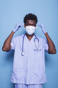 Portrait of doctor holding stethoscope against blue background