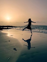 Silhouetted girl dancing at sunset on sandy beach, playa del risco, lanzerote, canary islands