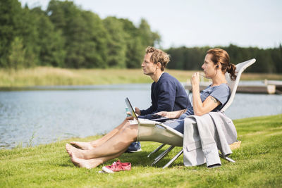 Full length side view of mature couple relaxing on desk chairs at lakeshore