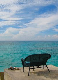 View of bench overlooking turquoise water against cloudy sky