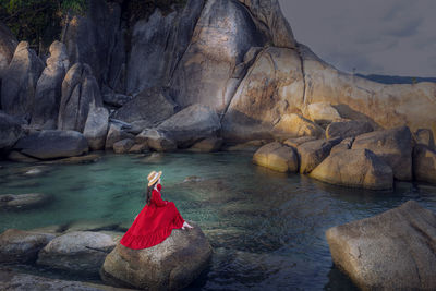 Young woman tourist in red dress sit on hin ta hin yai with blue sea and sky during summer travel 