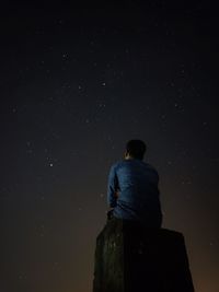 Low angle view of man sitting on rock against star field at night