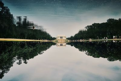Upside down image of historic building and lake against cloudy sky