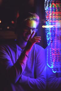 Smiling young man standing by illuminated glass window at night