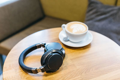 Photo of black wireless headphones and white cup of coffee on wooden table