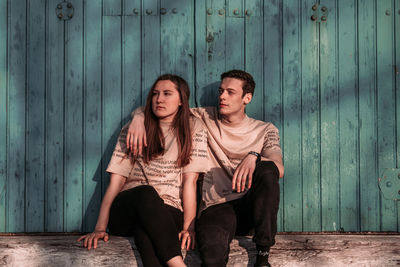 Portrait of young couple sitting against wall