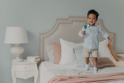 Boy holding lollipop while standing on bed at home