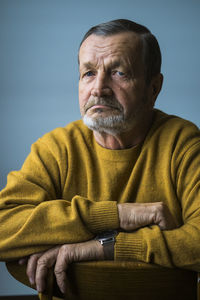 Portrait of senior man while sitting on chair against blue background