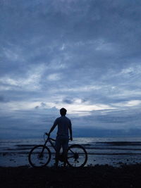 Rear view of silhouette man standing with bicycle at beach during dusk