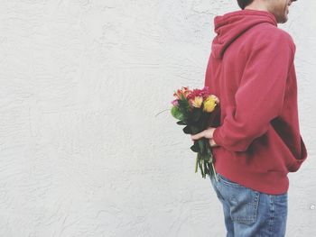 Midsection of man hiding flower bouquet back against wall