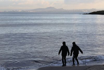 People walking on beach against sky during sunset