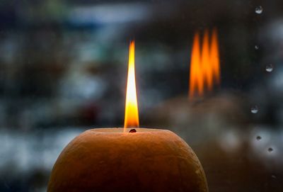 Close-up of burning candle by window