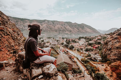 Side view of man looking at landscape while sitting on rock