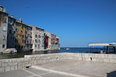 Residential buildings by sea against clear blue sky