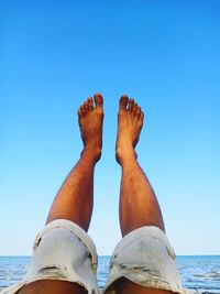 Low section of person against blue sea against clear sky