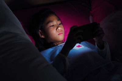 Girl using mobile phone on bed in darkroom