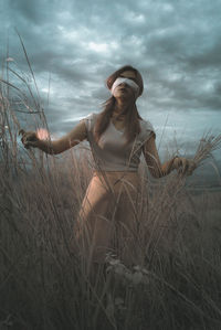 Woman with covered eyes walking on field against sky