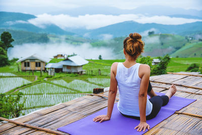 Rear view of woman sitting by lake against mountain