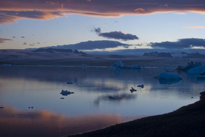 Scenic view of lake against cloudy sky during sunset