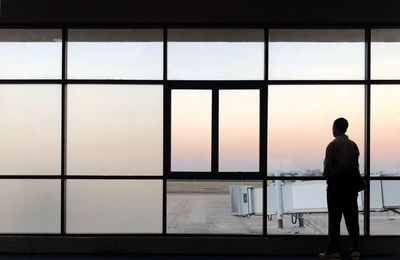 Rear view of silhouette man looking through window at airport