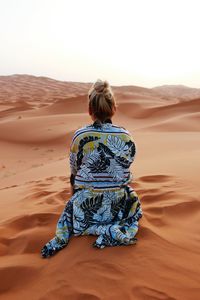 Rear view of woman sitting on sand dune