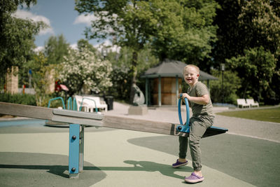 Full length side view portrait of happy boy with down syndrome enjoying seesaw at park