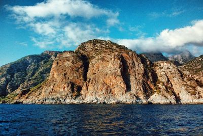 Scenic view of sea by mountain against sky