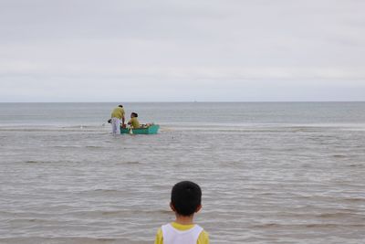 Rear view of friends standing on beach against sky