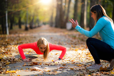 Woman doing push-ups, personal fitness trainer counting during training in the park.