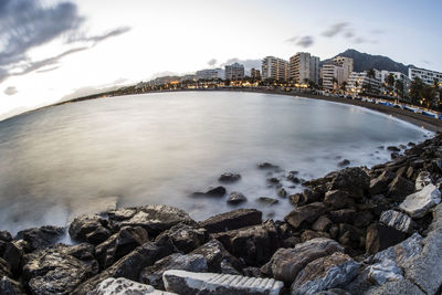 Sea by rocks in city against sky